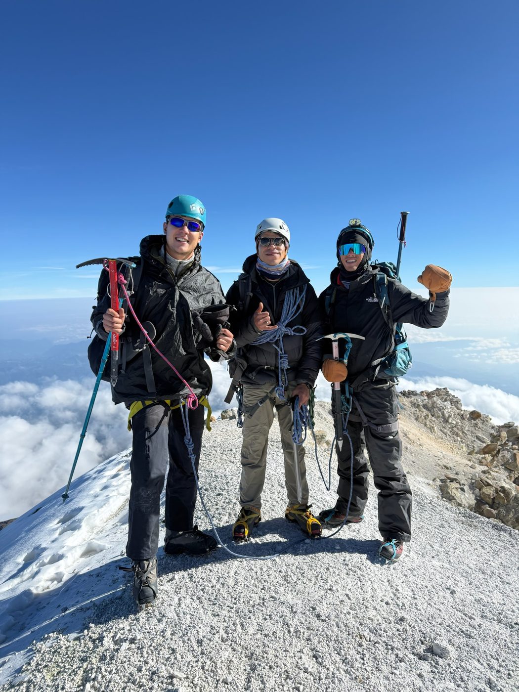 Three climbers on a glaciated summit above the clouds